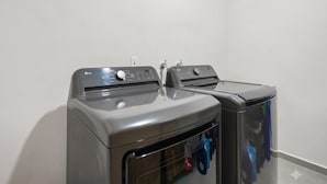 Two front-loading washing machines in a laundry room with a plain wall and a white floor. - Bahiban Residences by Monyxbnb (La Cruz de Huanacaxtle)