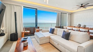 A modern living room with a large sofa, a wooden coffee table, a dining table with chairs, and a view of the ocean. - Bahiban Residences by Monyxbnb (La Cruz de Huanacaxtle)
