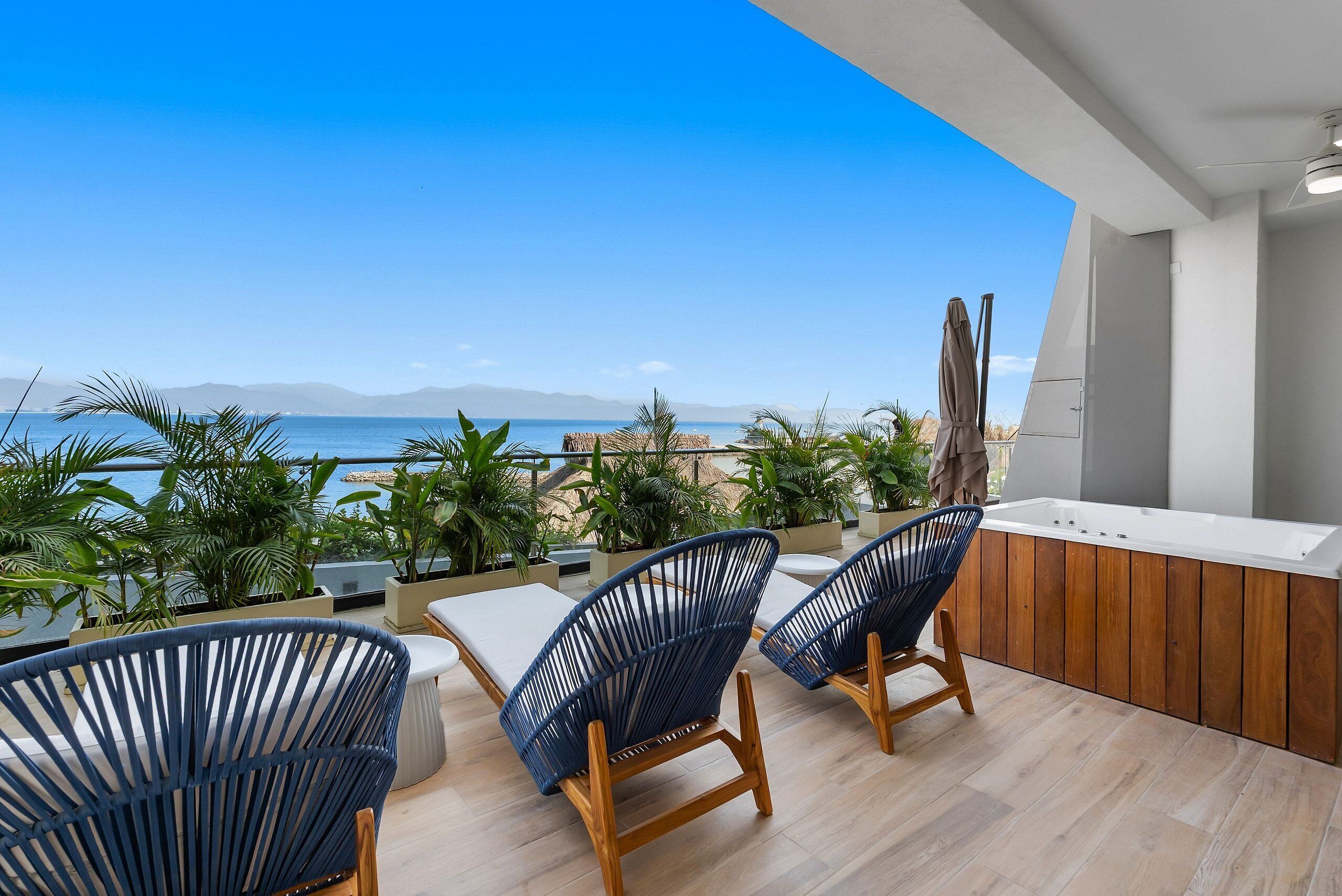 Een balkon met uitzicht op zee, twee blauwe stoelen, een houten tafel en een houten kast.