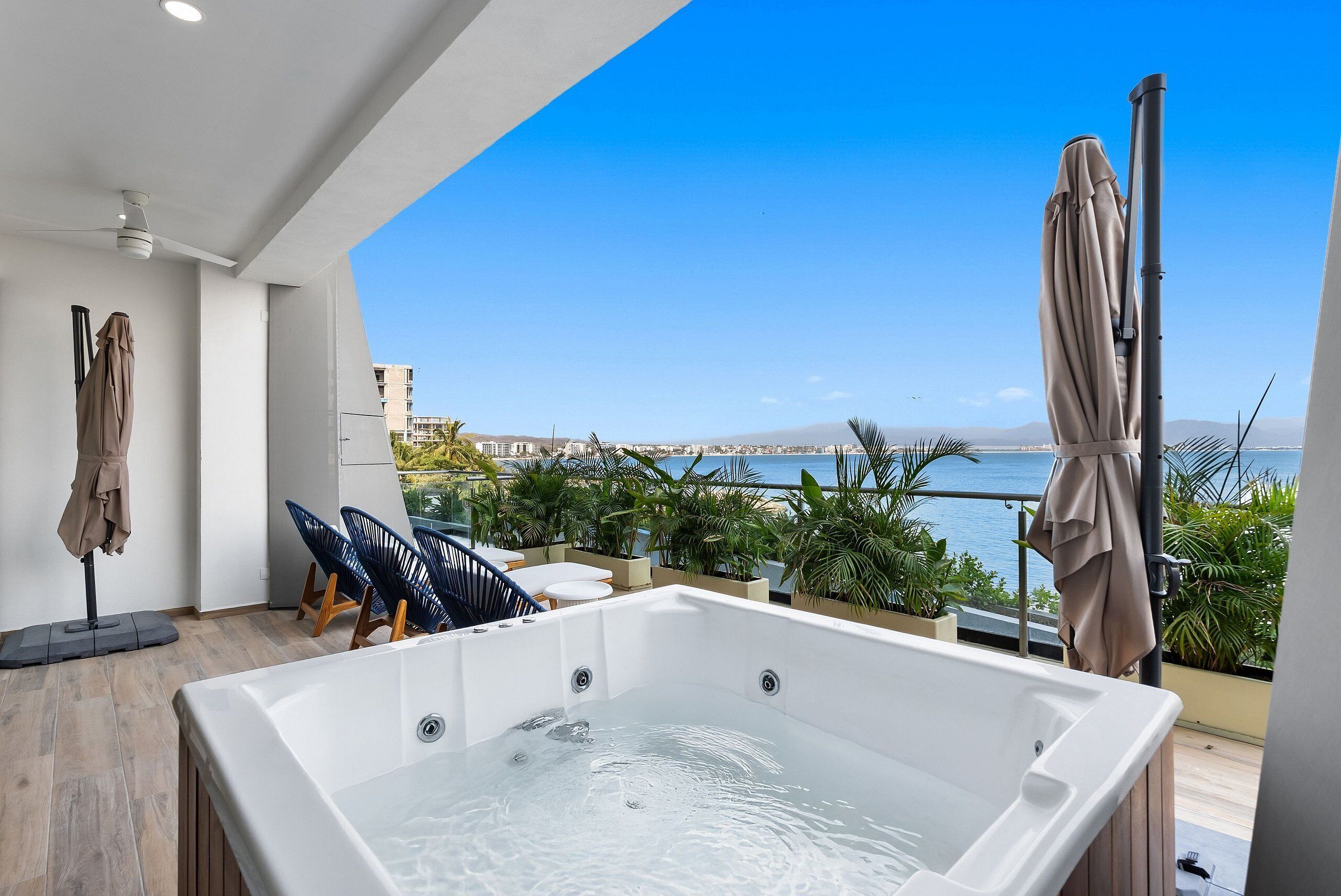 A modern outdoor hot tub with a city view, surrounded by lounge chairs and umbrellas.
