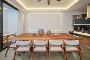Un comedor moderno con una mesa de madera, sillas blancas y una cocina al fondo.