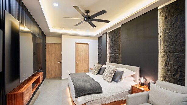 A modern bedroom with a bed, a TV, a ceiling fan, and a stone accent wall. - Bahiban Residences by Monyxbnb (La Cruz de Huanacaxtle)