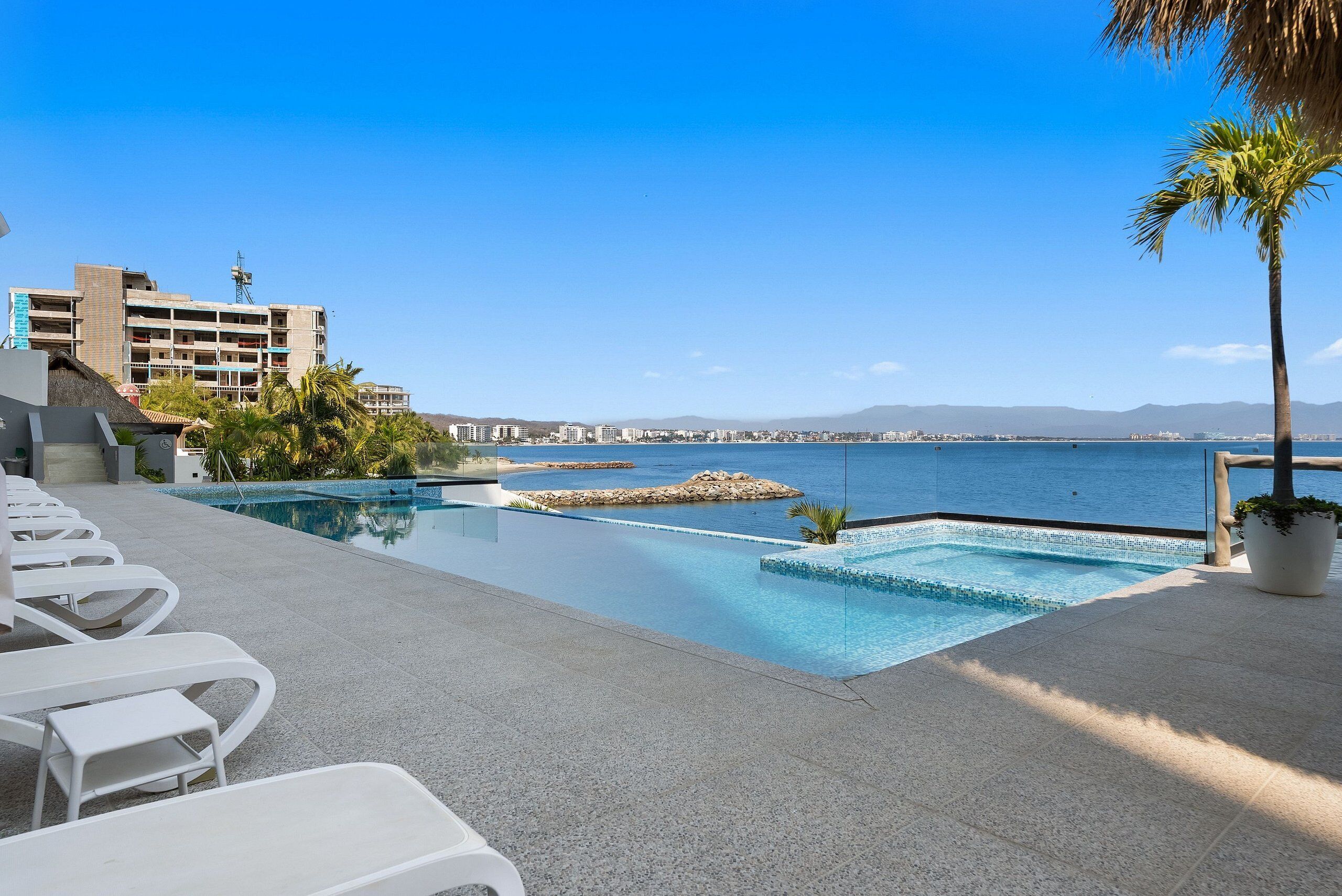 A pool area with lounge chairs and a view of the sea.