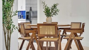 Een eetgedeelte met houten stoelen en een tafel, een potplant en een keuken op de achtergrond.