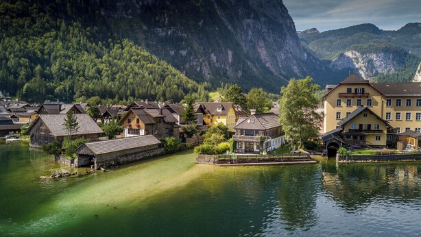 Un pueblo a orillas de un lago con casas de madera tradicionales, un muelle y montañas al fondo.