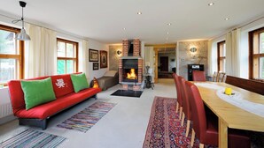 Una sala de estar moderna con chimenea, un sofá rojo, una mesa de comedor con sillas y vistas al exterior a través de amplios ventanales.