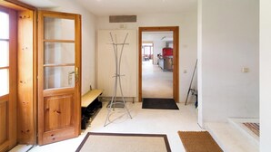 Un pasillo con puerta de madera, un banco, perchero y vista a una cocina.