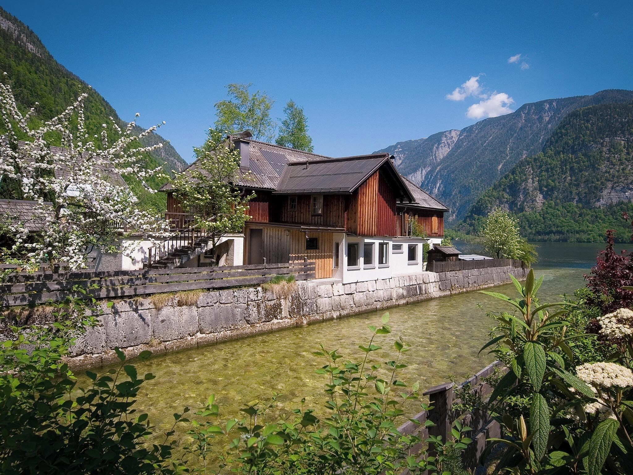Una casa de madera con un muro de piedra y un lago tranquilo al fondo.
