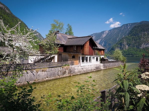 A wooden house with a stone wall and a clear lake in the background.