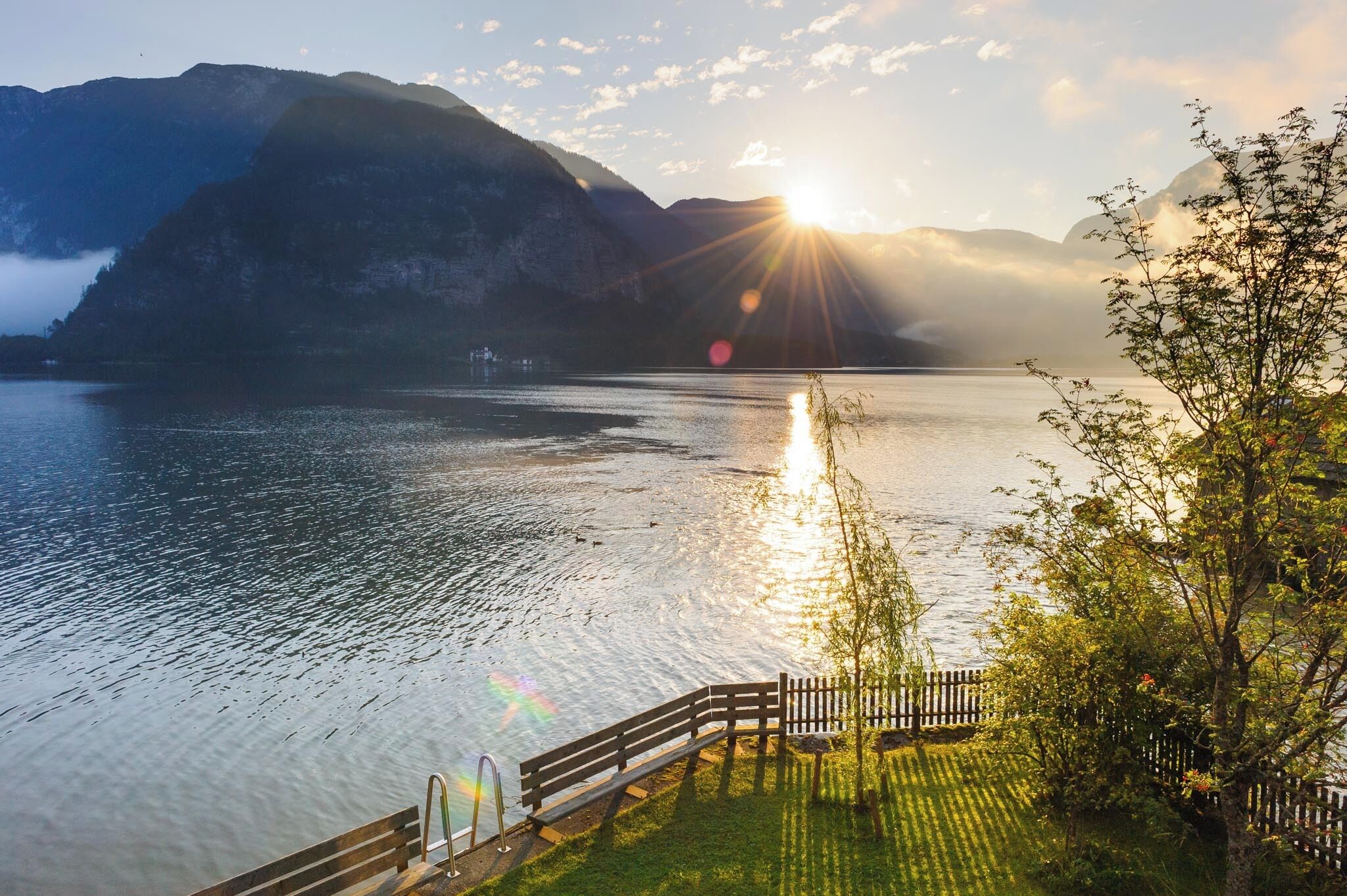 Une vue sur le lac, avec des montagnes en arrière-plan, une terrasse en bois et un banc.