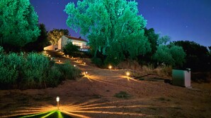 A nighttime landscape with a house, trees, and a pathway lit by ground lights. - Beira Baixa family retreat with mountain views, AC / breakfast! (Telhado)