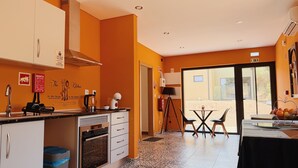 A kitchen with a coffee machine, kettle, and a microwave. There is a dining area with a table and chairs. The walls are orange, and there is a window with a view outside. - Beira Baixa family retreat with mountain views, AC / breakfast! (Telhado)