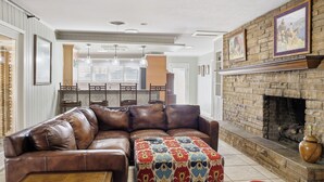 A living room with a leather sectional sofa, a patterned ottoman, a fireplace, and framed artwork on the wall. - Right at Home-Midland Home away from Home with Billiards (Midland)