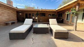 An outdoor patio with two lounge chairs, a small table, and a brick wall. - Right at Home-Midland Home away from Home with Billiards (Midland)