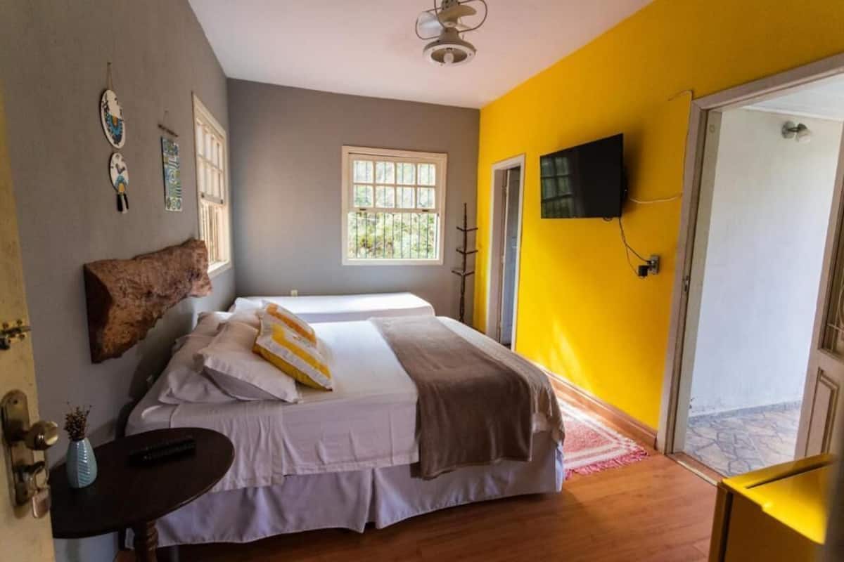 Un dormitorio con una cama, televisor, ventana y puerta que da a un balcón.