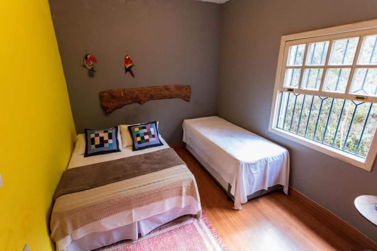 Una habitación con una cama, dos camas individuales, un ventanal con vistas y un cabecero de madera.
