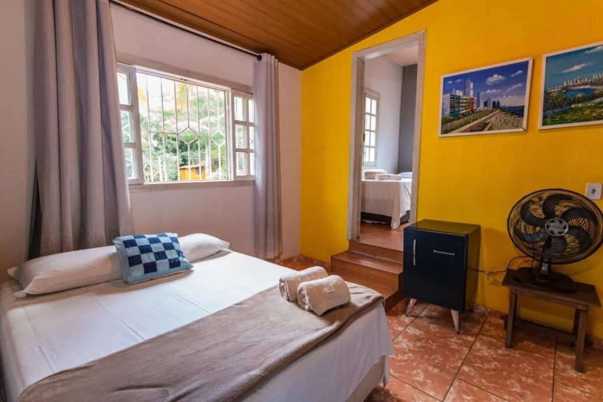 Habitación de hotel con cama, escritorio, ventilador y ventana con cortinas.