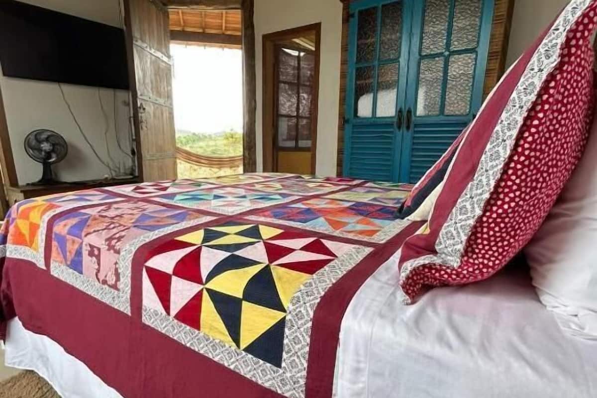 Un dormitorio con un edredón colorido, techo de madera, puerta azul y un ventilador.