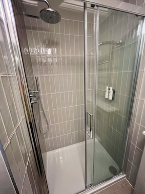 Eine Duschkabine mit Glaswänden, einer Handbrause, einer Glastür und einer gefliesten Wand.