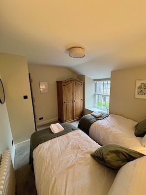 Une chambre avec deux lits, une armoire en bois, un radiateur et une fenêtre donnant sur un beau paysage.