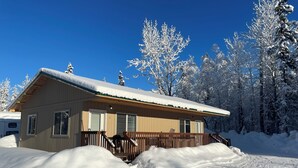 En stuga av trä med en veranda, omgiven av snötäckta träd.