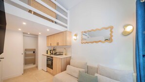 Un espacio habitable compacto con kitchenette, un sofá con cojines, techo de madera y un espejo montado en la pared.