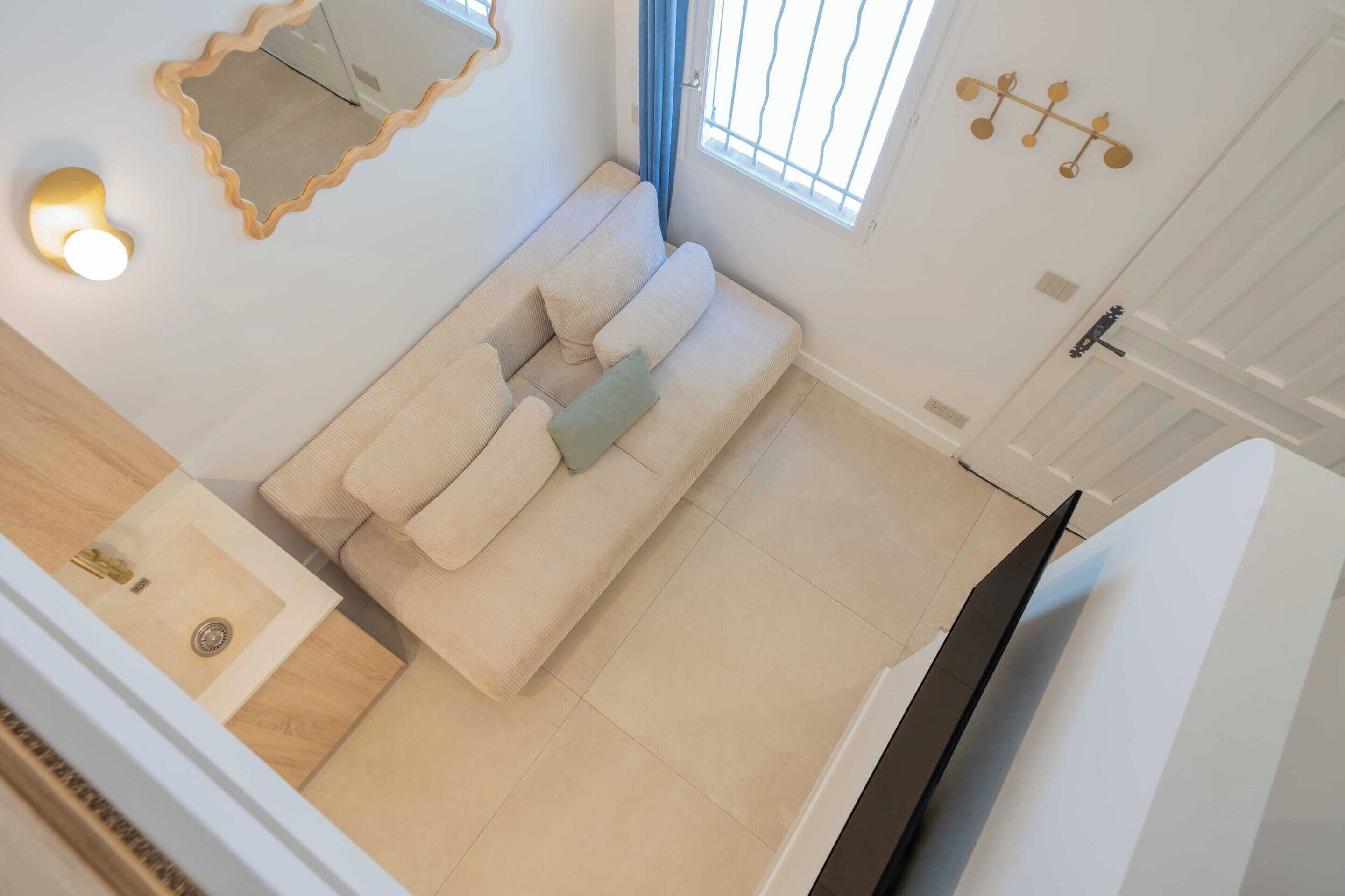 A room with a sofa, a mirror, a light fixture, a window with blinds, and a door with a handle.