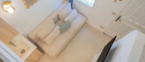A room with a sofa, a mirror, a light fixture, a window with blinds, and a door with a handle.