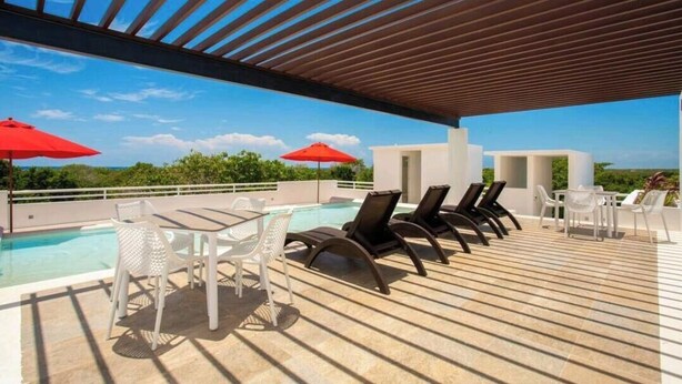 Zona de piscina al terrat amb gandules i ombrelles, taula de bitlles i una vista despejada del cel.
