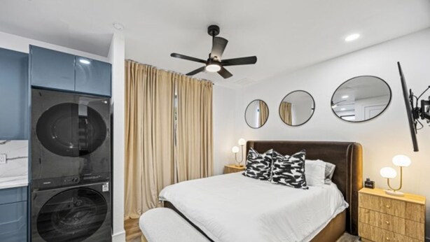Een slaapkamer met een bed, nachtkastjes, een plafondventilator en een wasmachine.