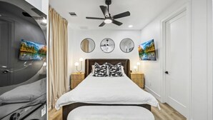 Een slaapkamer met een bed, een plafondventilator, drie spiegelwanden en kunst aan de muren.