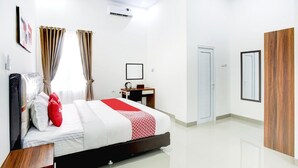 A modern hotel room with a bed, a desk, a chair, a wardrobe, and an air conditioning unit. - Stylish Double Suite Escape with Parking Access (Bandar Lampung)