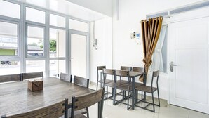 A dining area with a wooden table and chairs, large windows, and a white door with curtains. - Stylish Double Suite Escape with Parking Access (Bandar Lampung)