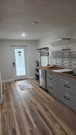 A kitchen with wooden flooring, a dishwasher, a sink, and a door with a frosted glass panel. - Angella Ct Getaway - Sleeps 6 - Near Downtown (McMinnville)