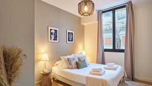 Quarto com cama, abajures, janela com cortinas e quadros na parede.