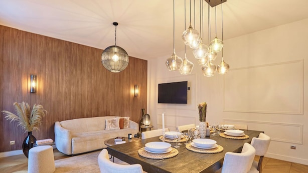 Uma área de refeições com mesa de madeira, cadeiras brancas e luminárias pendentes.