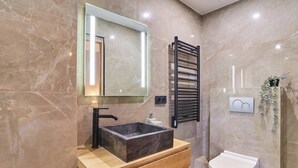 Uma casa de banho com lavatório de mármore, um espelho, um porta-toalhas e uma sanita.