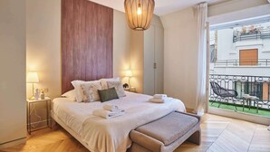 Quarto com cama, abajures, painel de parede de madeira, luminária pendente e vista para uma varanda.