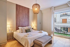 Une chambre à coucher avec un lit, des lampes de chevet, un mur recouvert de panneaux en bois, un luminaire suspendu et une vue sur le balcon.
