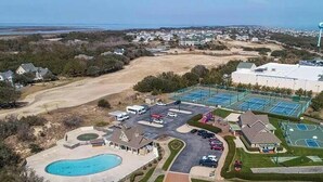 Vue aérienne d’un quartier résidentiel avec un grand immeuble, une piscine, des courts de tennis et un parking.