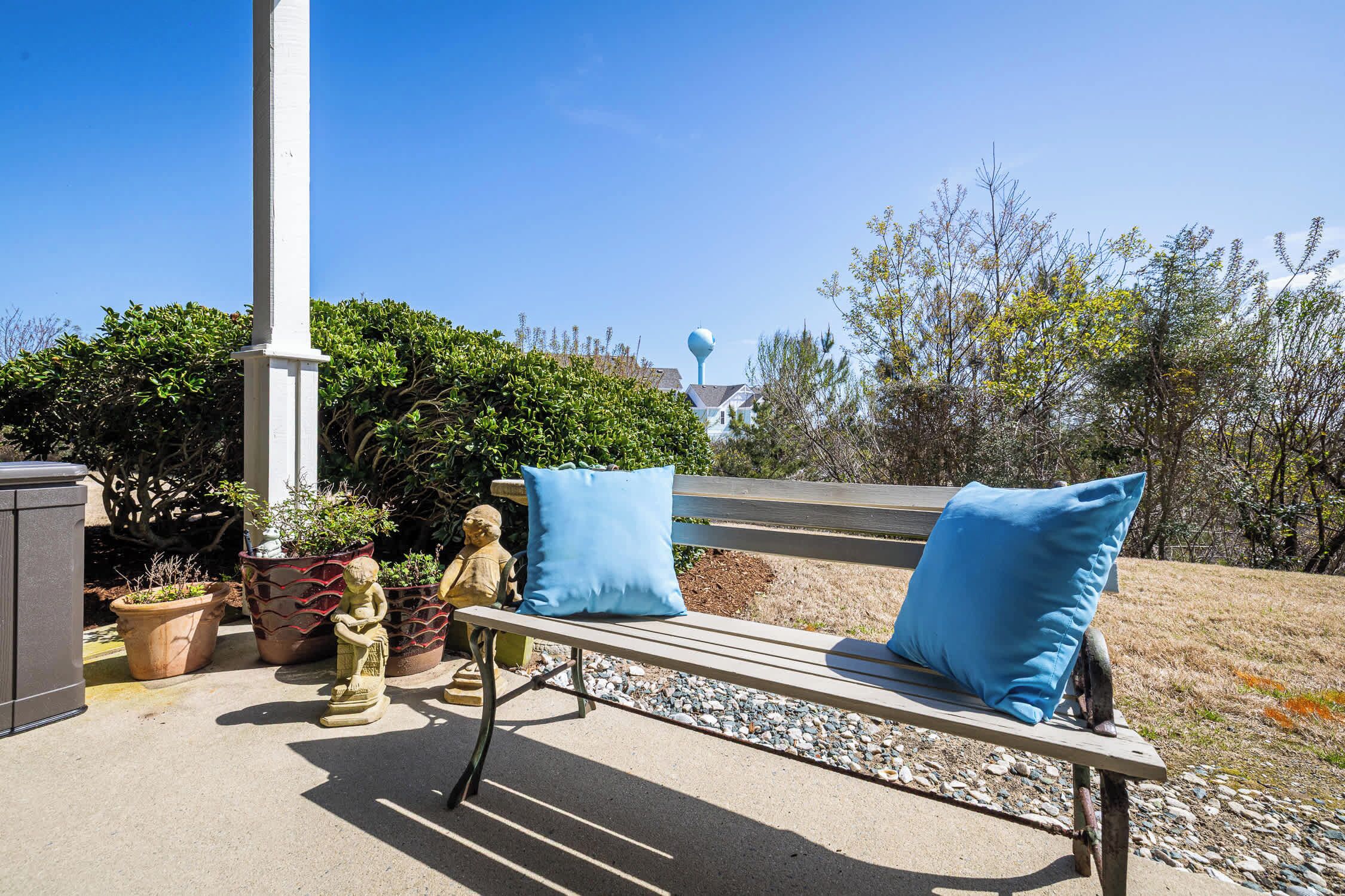 A bench with blue cushions, a white column, and potted plants.