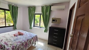 Ein Schlafzimmer mit Bett, Schminktisch, Klimaanlage und einem Vorhangfenster.