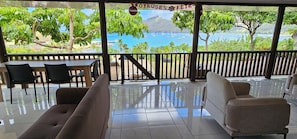 A covered outdoor seating area with a table and chairs, a sofa, and a view of the sea and mountains.