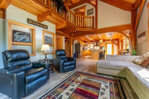 A spacious living room with a fireplace, leather chairs, a sofa, and a wooden staircase.