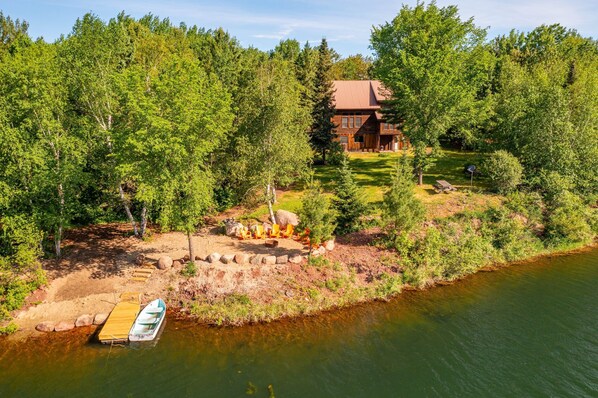 A cabin by a lake surrounded by trees, with a dock and outdoor seating area.