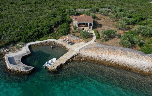 An aerial view of a coastal property with a stone pier leading to a clear blue harbor, a small boat docked at the pier, and a house with a red roof surrounded by greenery. - Beautiful home in Tkon with WiFi (Tkon)