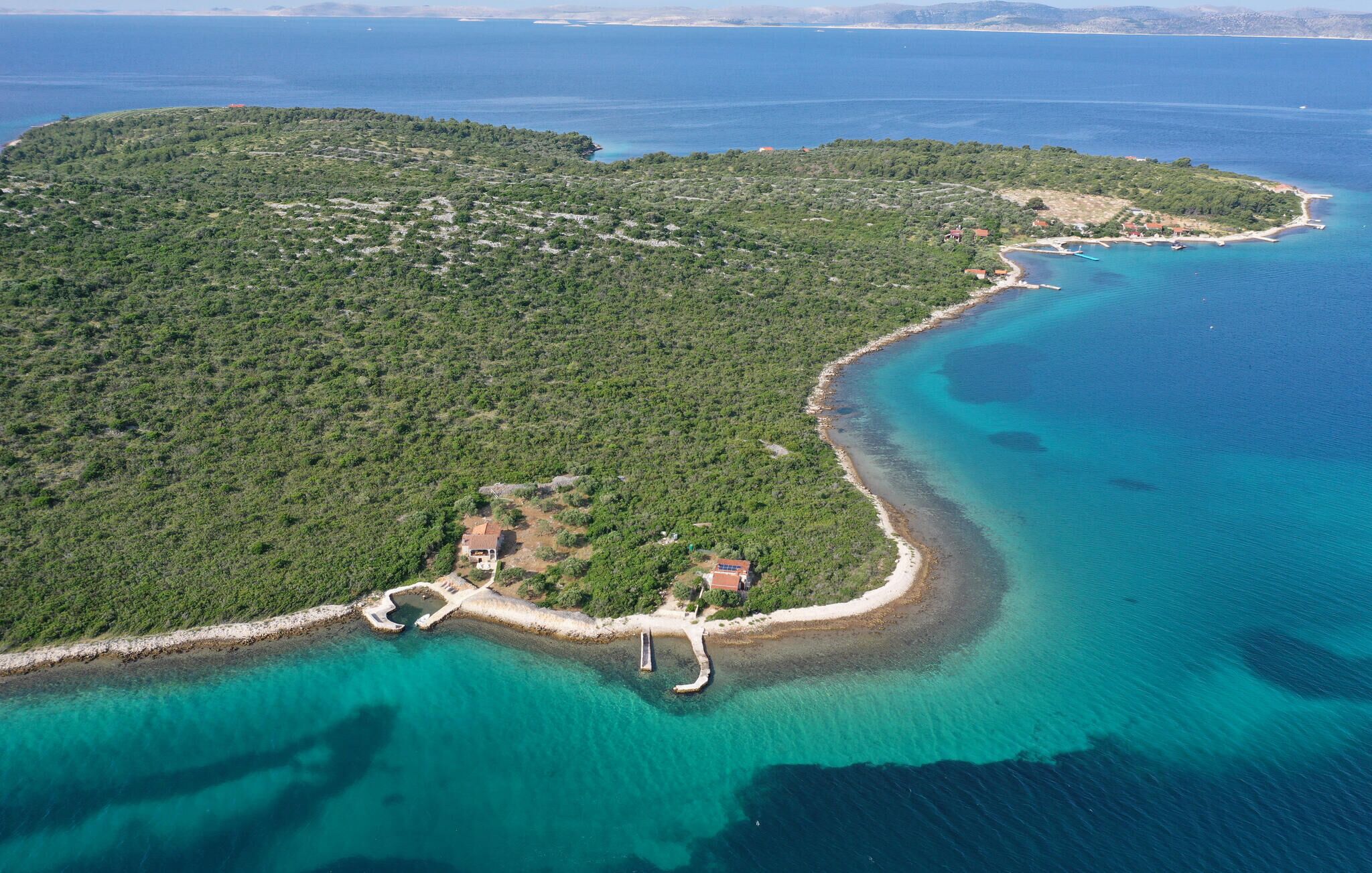 An aerial view of a coastal area with a small island, clear turquoise waters, and sparse vegetation.