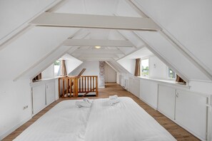 Un dormitorio con techo inclinado, piso de madera, una cama con ropa de cama blanca, un banco de madera y una pared de piedra.