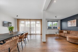 A modern living room with a dark wooden dining table, cushioned chairs, a brown sofa, and a large window with sheer curtains. - Spacious holiday home in the center of Langweer (Langweer)