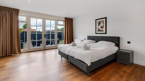 A bedroom with a large bed, a nightstand, a framed picture, and a sliding glass door leading to an outdoor area. - Spacious holiday home in the center of Langweer (Langweer)